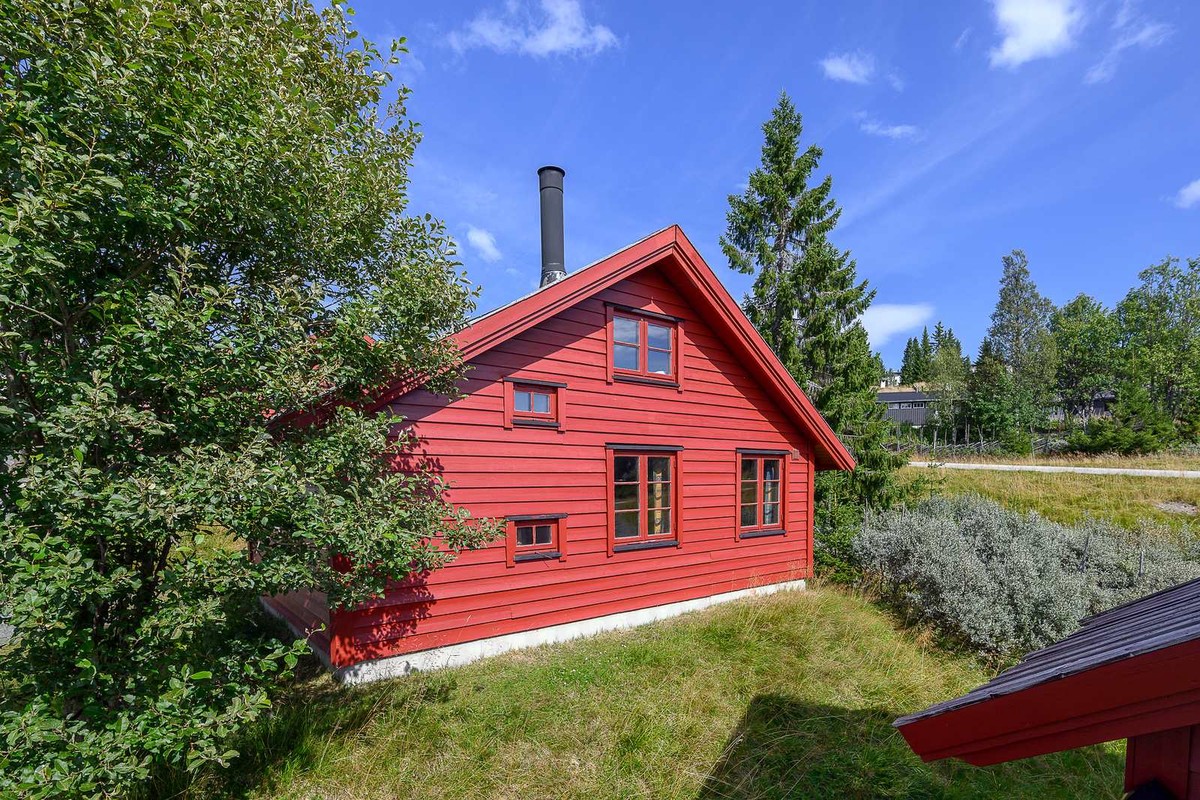 Rød fjellhytte på Lillehammer fjellstue med blå himmel bak og grønne trær foran