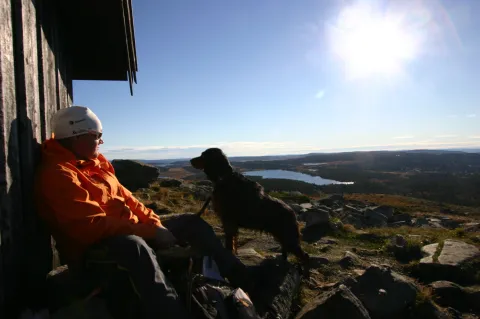 person med hund på fjell med vann i bakgrunnen